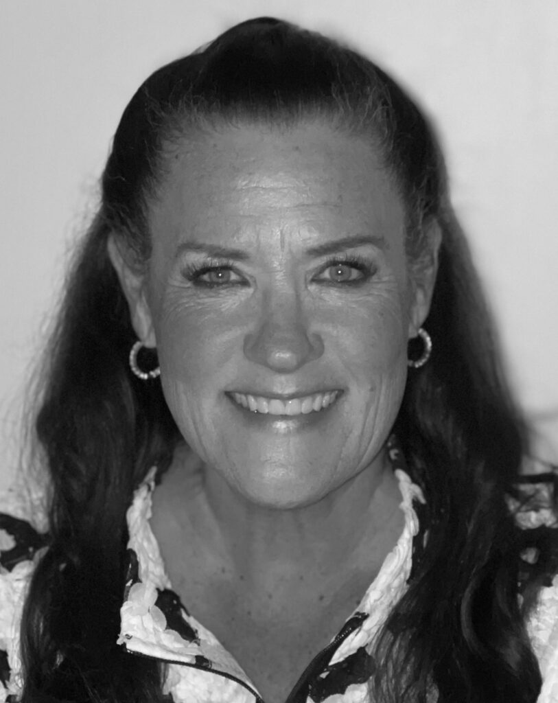 Black-and-white headshot of Susan Flinn Cobian smiling, long wavy hair, hoop earrings